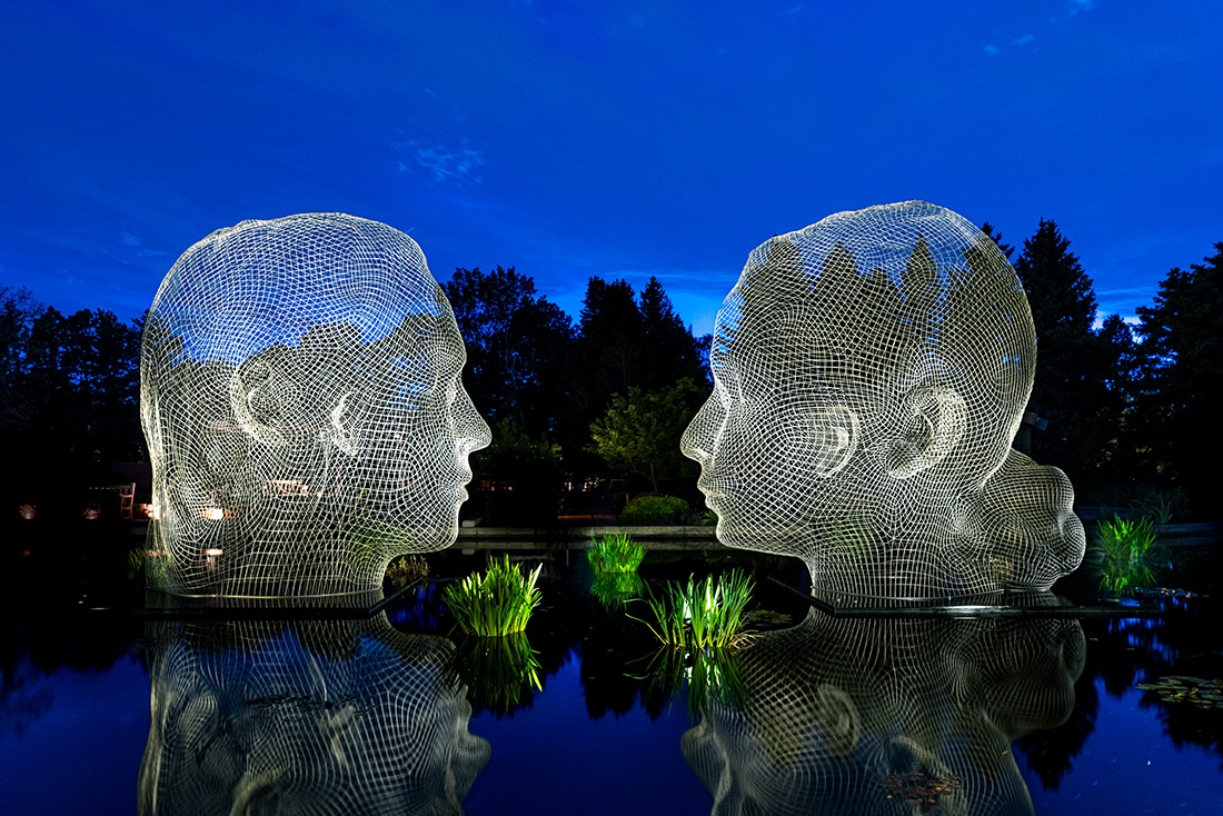Two sculptures of faces sitting in water and luminated by lights
