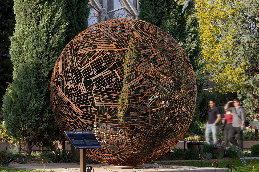 Large round steel sculpture displayed outside, with notes carved in the steel.