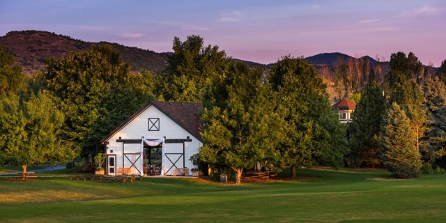 White stables with trees behind them at sunset