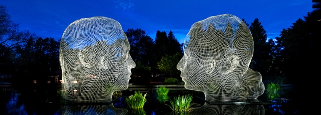 Two sculptures of faces sitting in water and luminated by lights