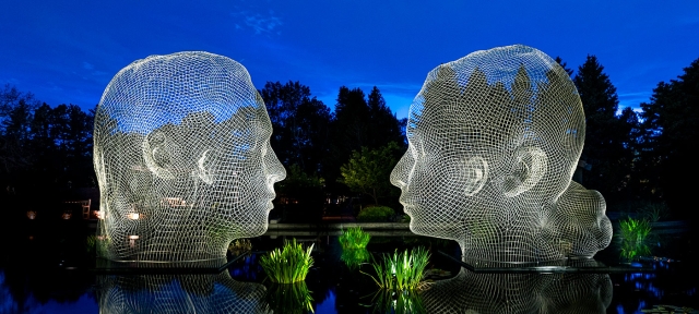 Two sculptures of faces sitting in water and luminated by lights