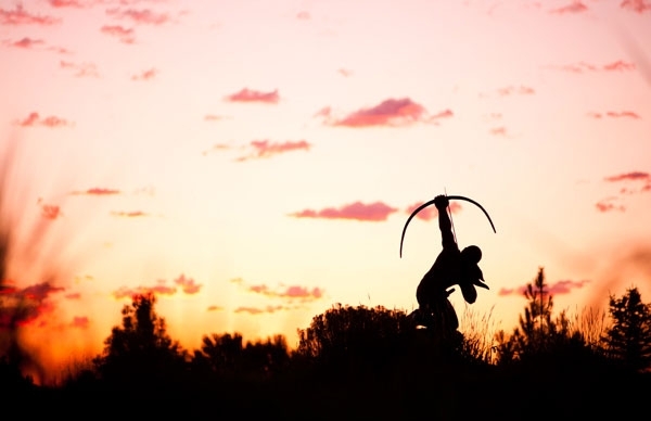 sculpture of man shooting arrow into air in front of sunset backdrop