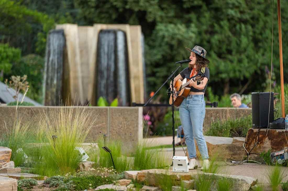 Person wearing a hat, singing and playing a guitar at Evenings al Fresco