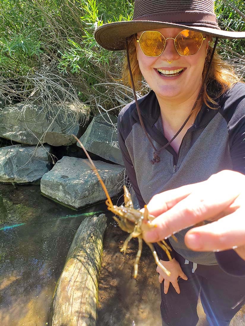 Person in sunhat holding small crayfish in front of creek