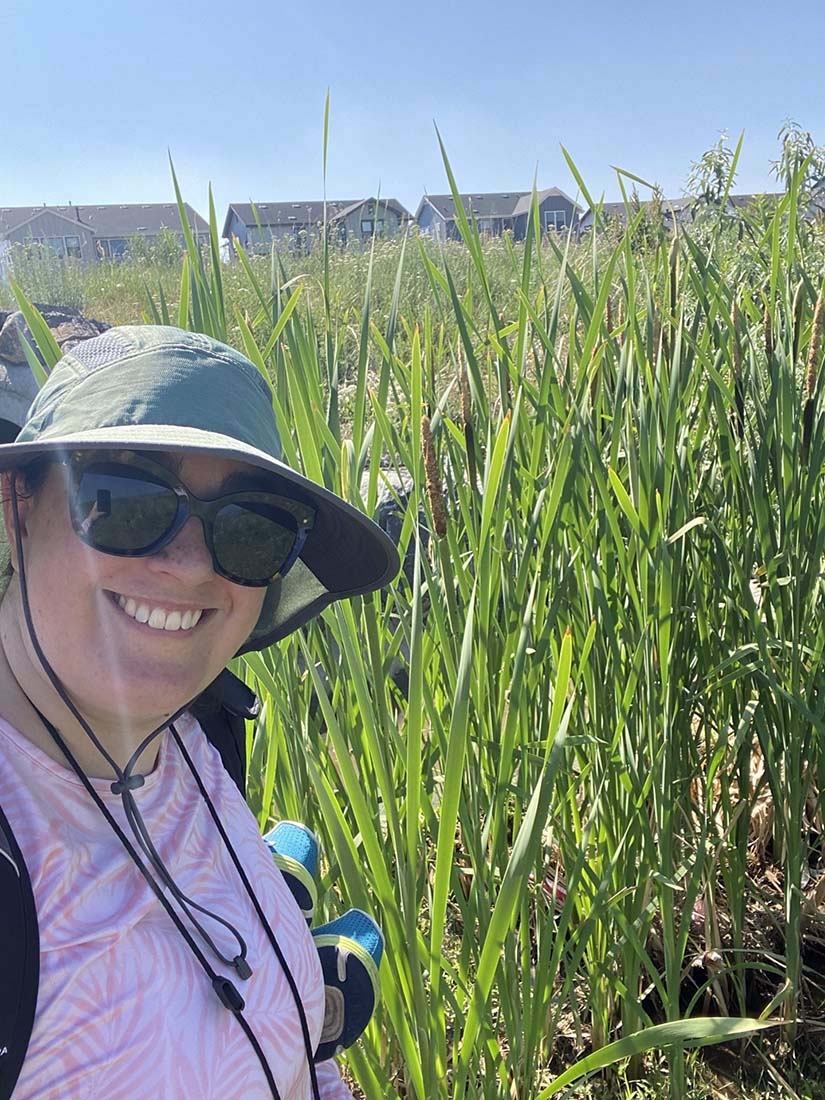 Person in foreground in hat and glasses with tall grass behind them