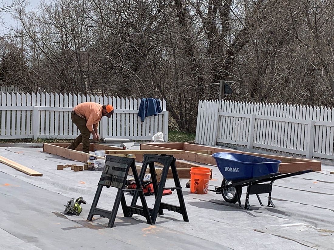 sawhorses in foreground and man in background installing raised garden beds