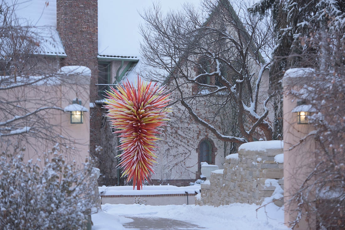 Glass Chihuly sculpture in front of snowy mansion