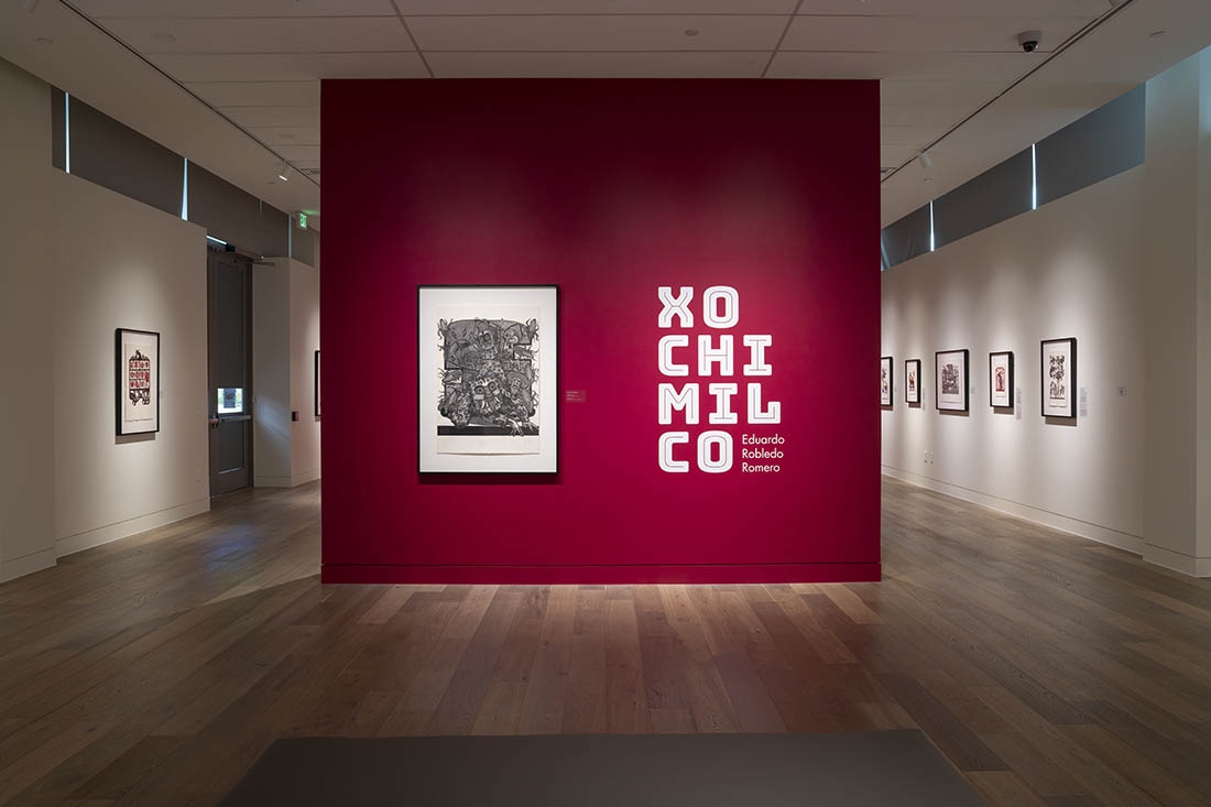 A red exhibit wall with white text and an artwork
