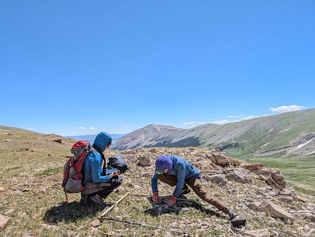 Two scientists on mountainous terrane with mountains in background