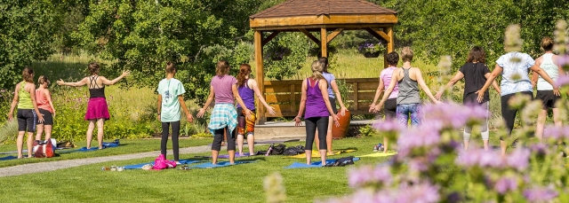 People doing yoga outside in a grassy field with a gazebo in the background