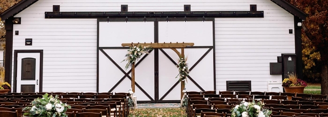 The outside of a white barn with chairs facing the barn