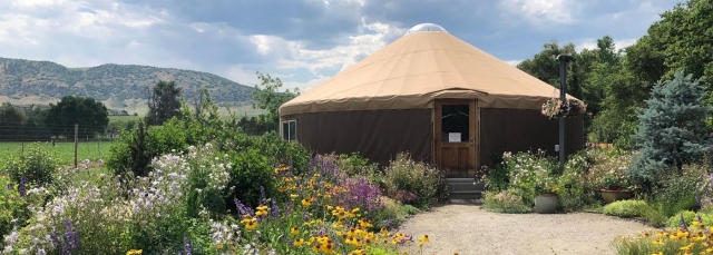 Flower gardens surrounding a yurt with white clouds and a blue sky